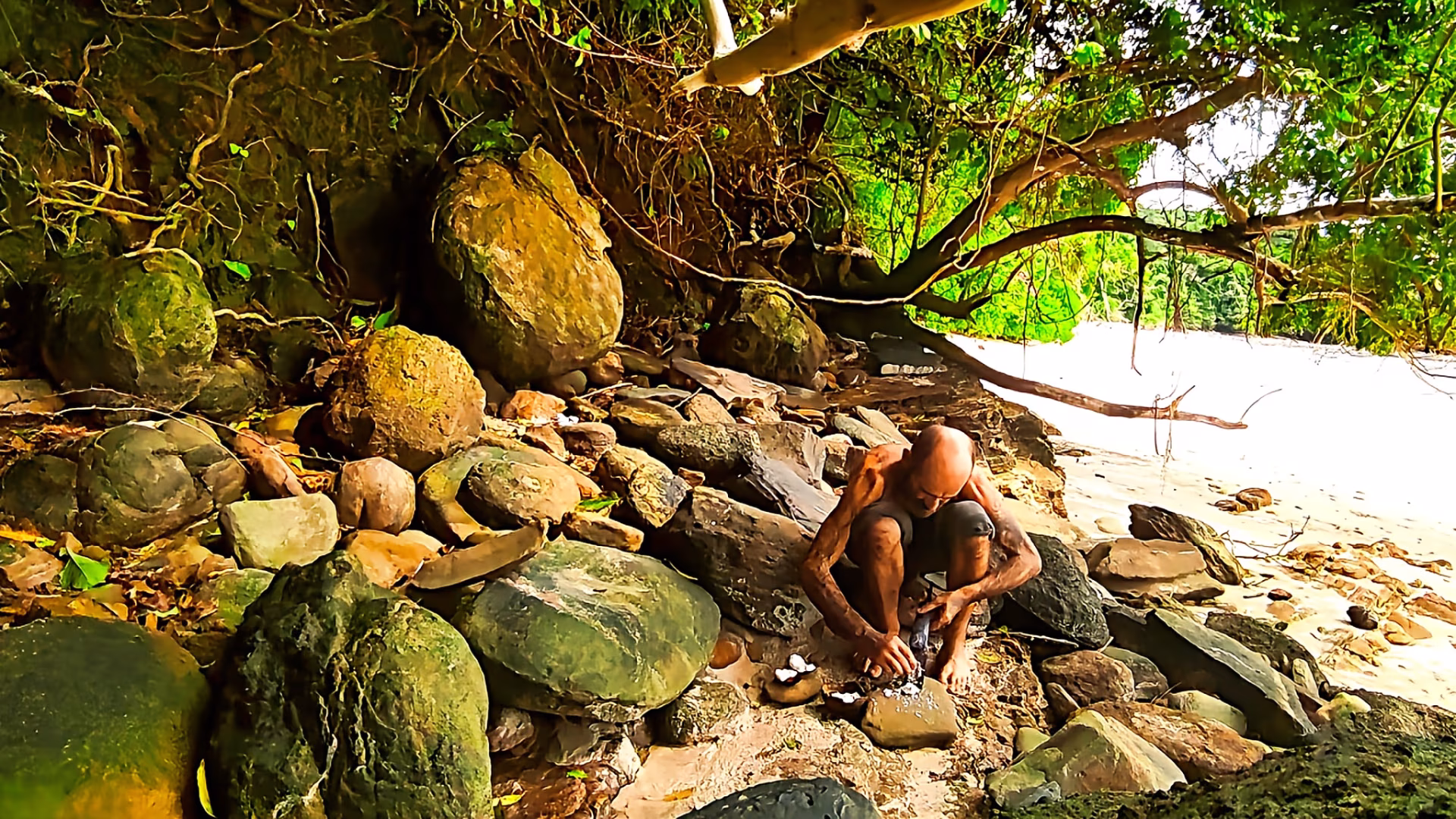 Un homme assis sur des rochers qui mange des noix de coco